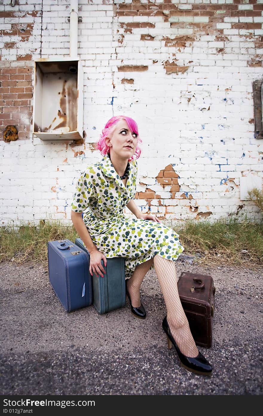 Woman with pink hair wearing polka dot dress in alley with suitcases. Woman with pink hair wearing polka dot dress in alley with suitcases