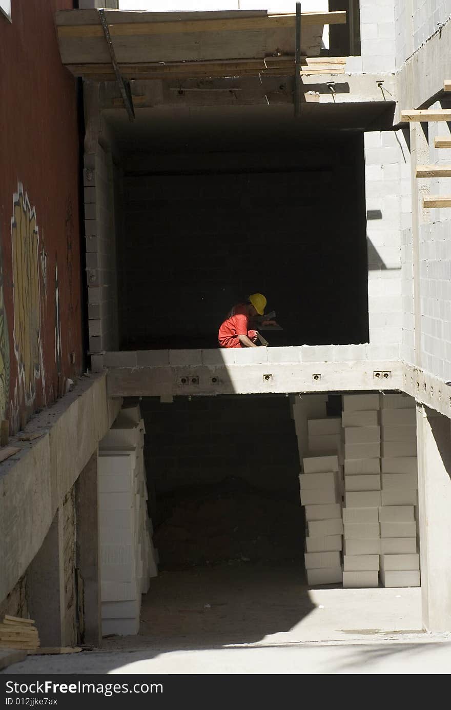 Worker Squats on Floor of Jobsite - Vertical