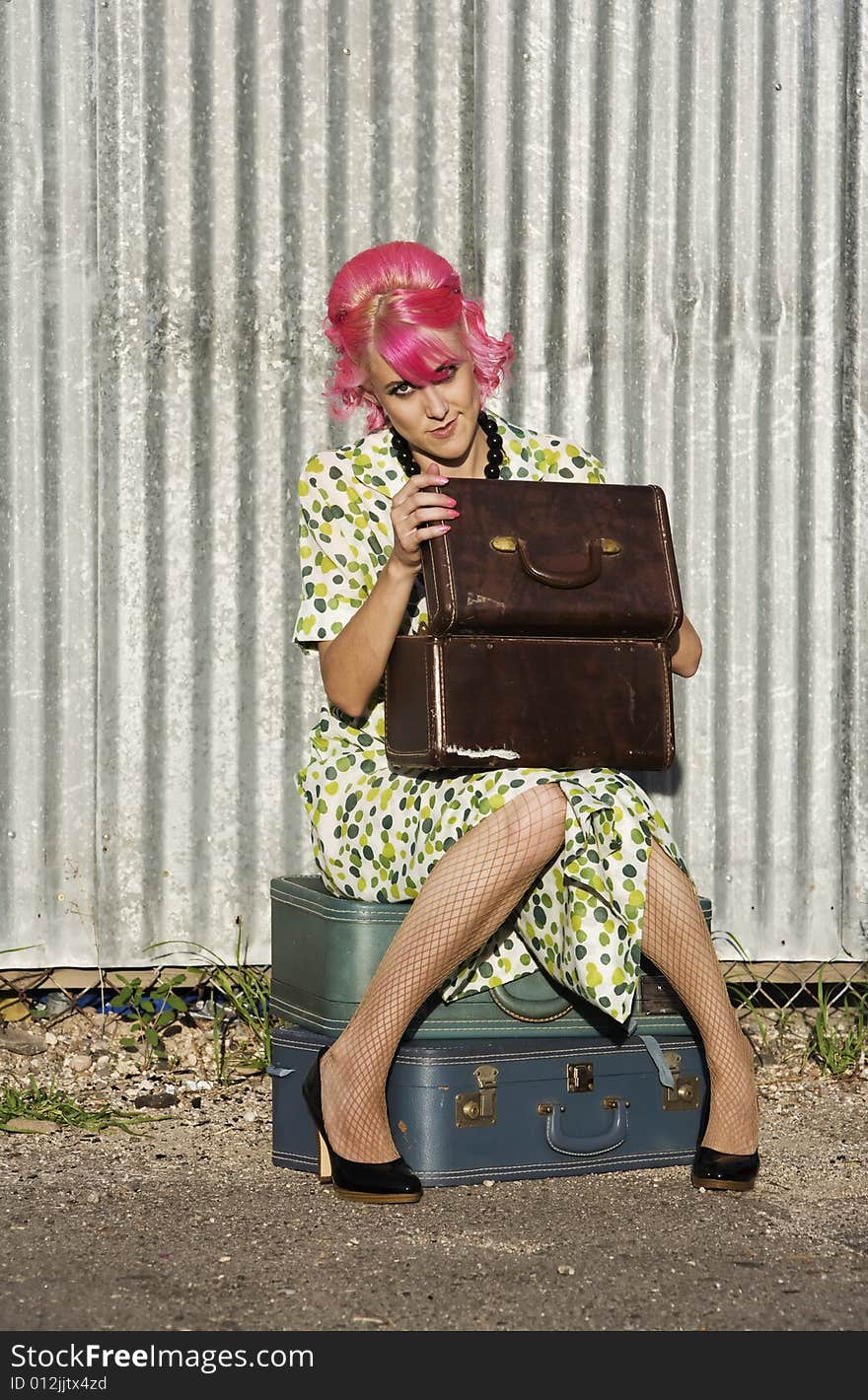 Woman with pink hair wearing polka dot dress in alley with suitcases. Woman with pink hair wearing polka dot dress in alley with suitcases