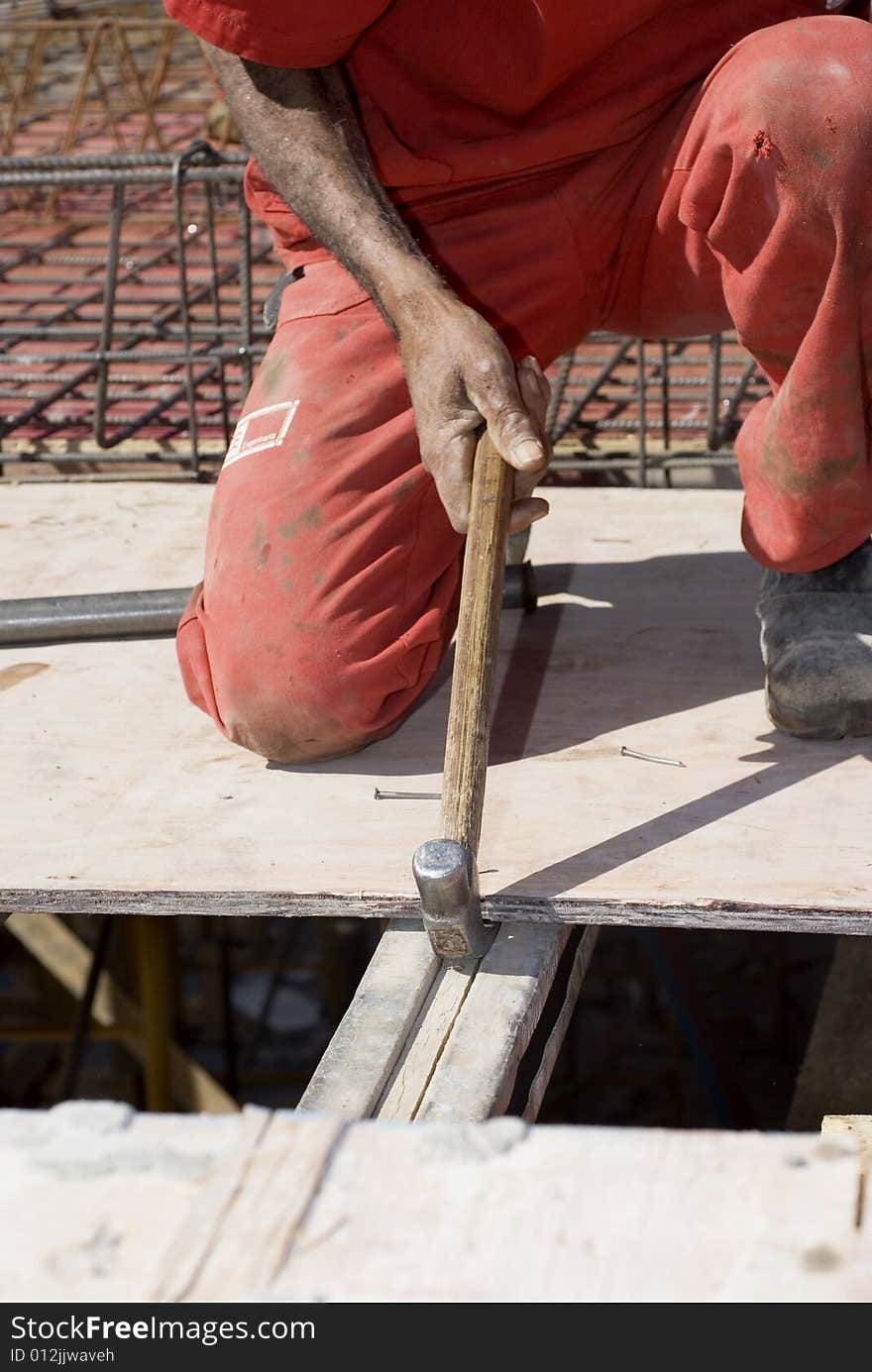 Construction worker pulling board with hammer. He is kneeling on the board. Vertically framed photo. Construction worker pulling board with hammer. He is kneeling on the board. Vertically framed photo.