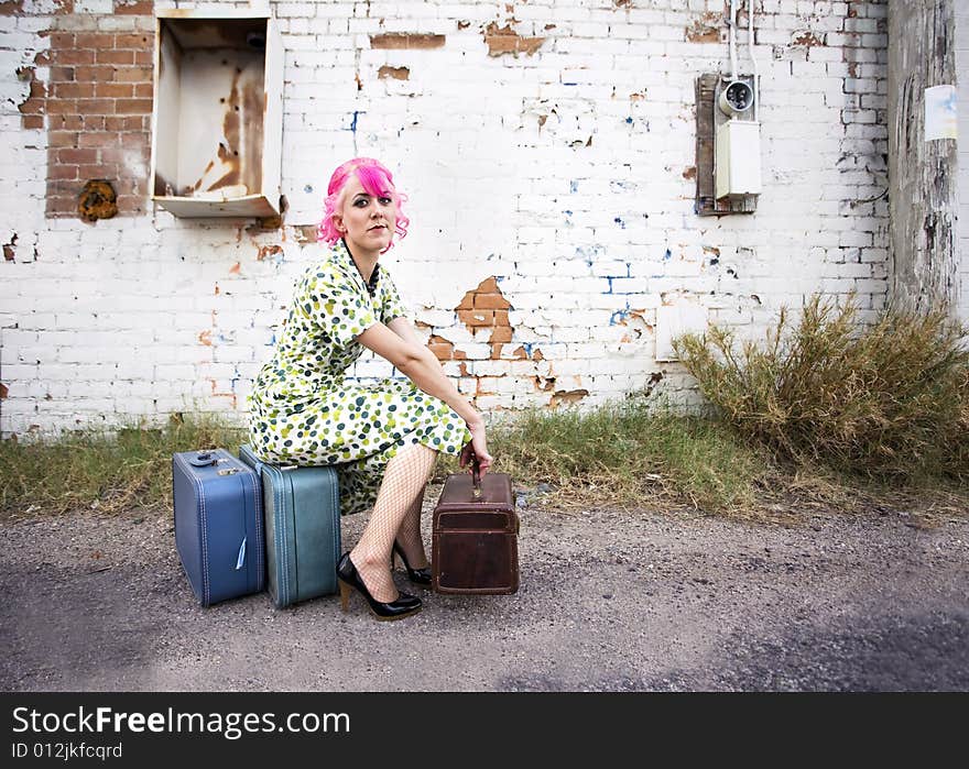 Woman with pink hair wearing polka dot dress in alley with suitcases. Woman with pink hair wearing polka dot dress in alley with suitcases