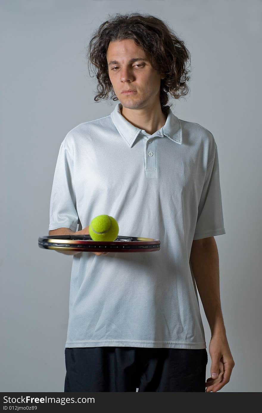 Male athlete holding a tennis racket and balancing a ball on it.  He is looking at the tennis ball.  Vertically framed shot. Male athlete holding a tennis racket and balancing a ball on it.  He is looking at the tennis ball.  Vertically framed shot.