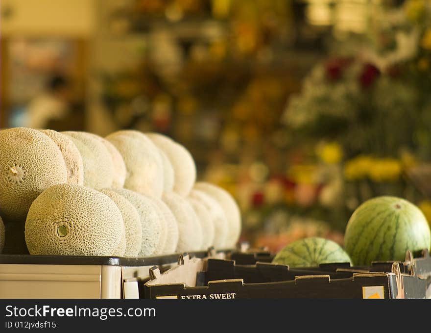 A stack of cantelopes and round watermelons in a grocery with flowers in the background. A stack of cantelopes and round watermelons in a grocery with flowers in the background.