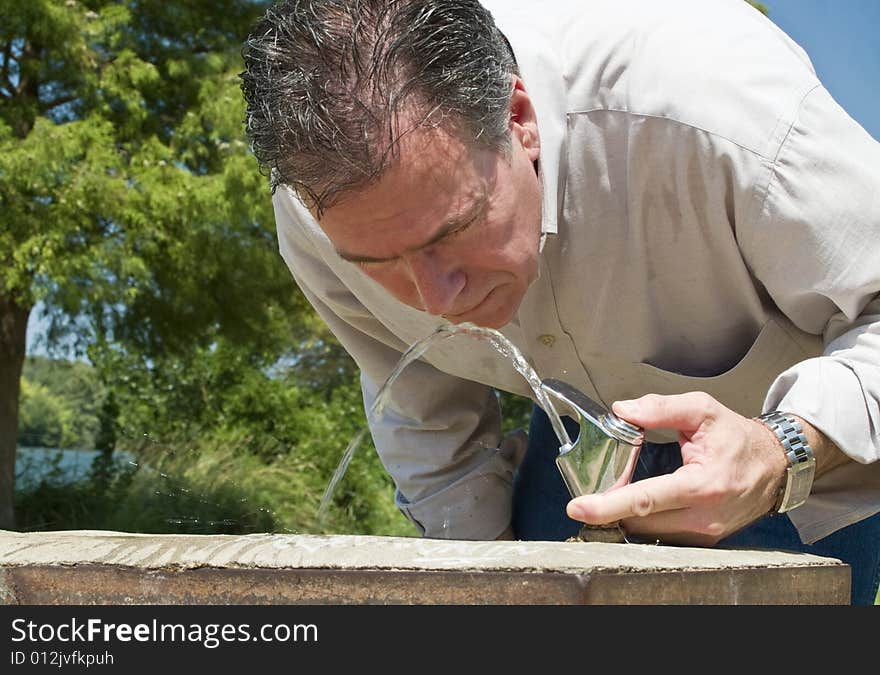 A man drinking water from a park water fountain no a very hot summer day. A man drinking water from a park water fountain no a very hot summer day.