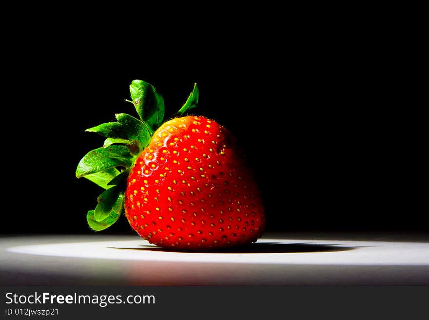 Lucious, ripe, red , juicy strawberry highlighted by a single spotlight against a dark background.