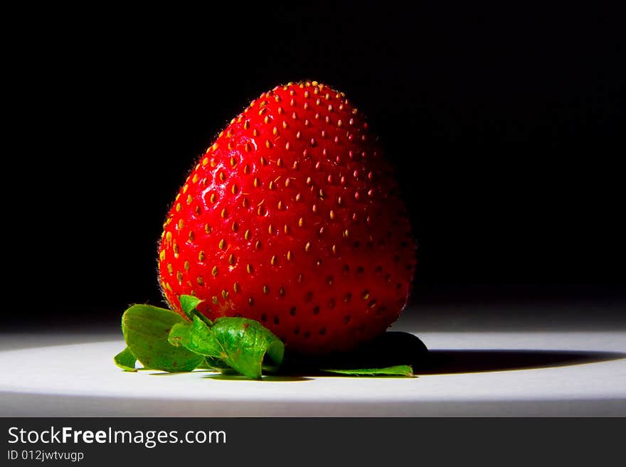 Lucious, ripe, red , juicy strawberry highlighted by a single spotlight against a dark background.