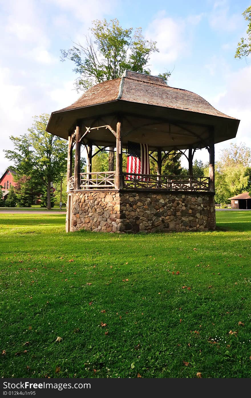 A rustic stone and wood bandstand in a small town park decorated with an American flag. A rustic stone and wood bandstand in a small town park decorated with an American flag.