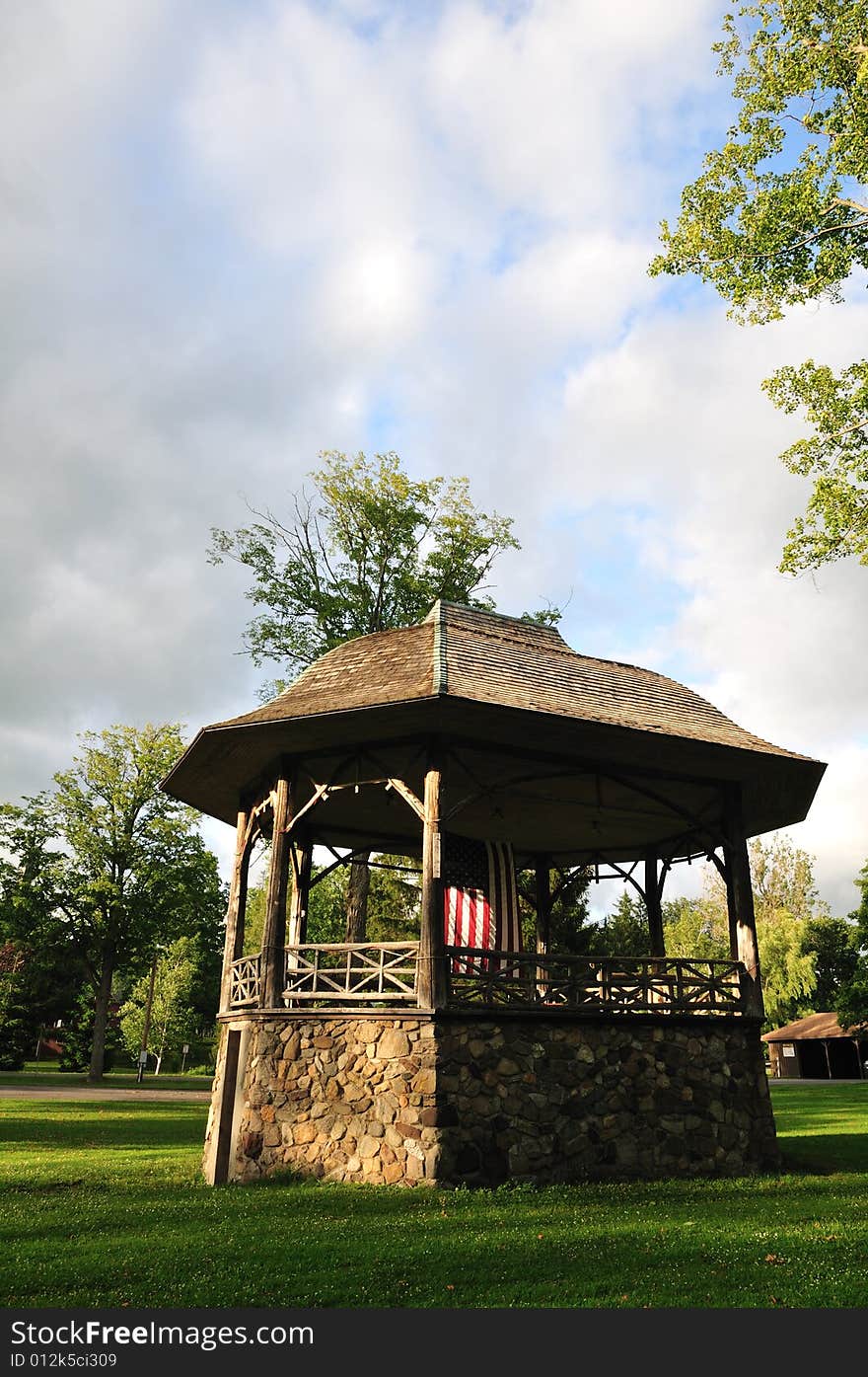 A rustic stone and wood bandstand in a small town park decorated with an American flag. A rustic stone and wood bandstand in a small town park decorated with an American flag.