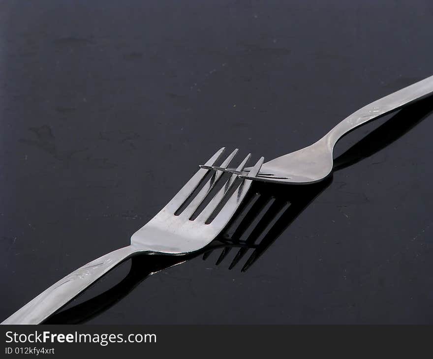 Two silver forks on a black shiny surface. Two silver forks on a black shiny surface