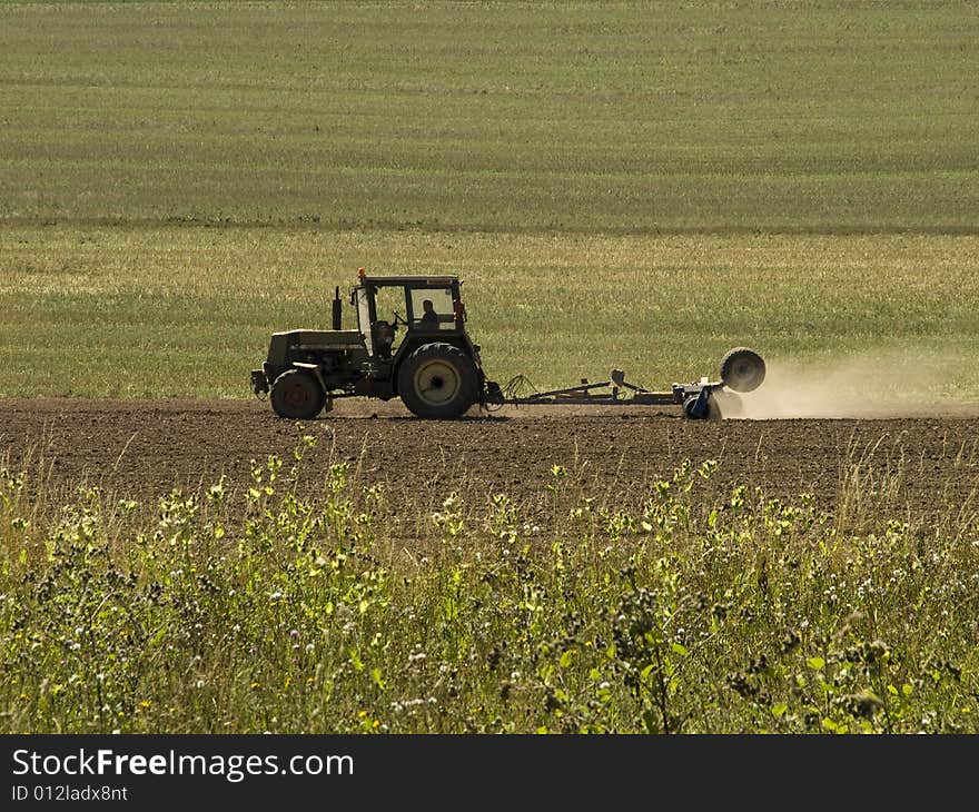 Green tractor drilling a field at summer time producing a lot of dust. Green tractor drilling a field at summer time producing a lot of dust