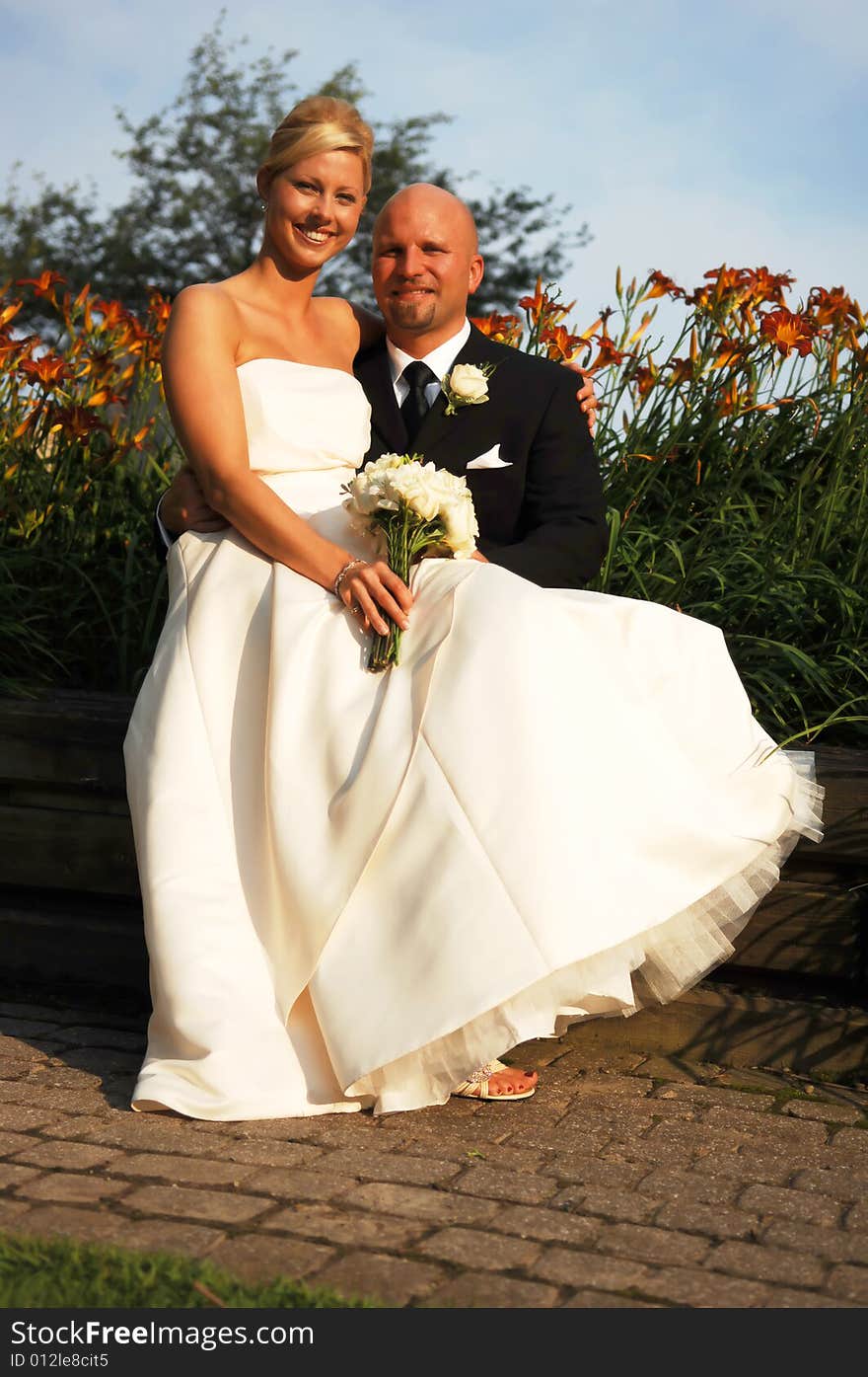 An just married couple sitting on a bench at sunset for a photo shoot. An just married couple sitting on a bench at sunset for a photo shoot.