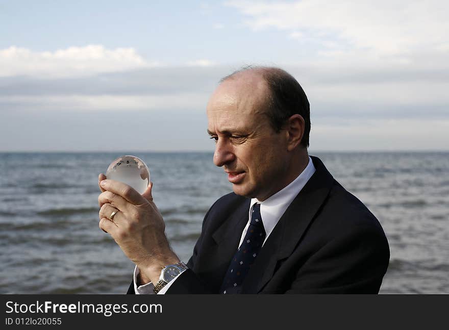 Man holding a crystal globe of the earth in his hands with the ocean in the back ground. Man holding a crystal globe of the earth in his hands with the ocean in the back ground.