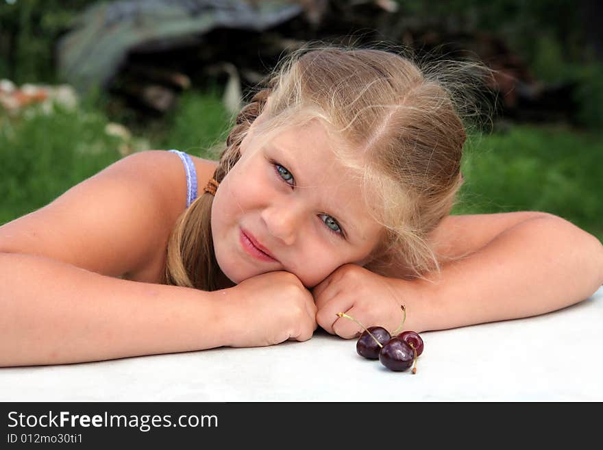 Pretty blond girl sitting near a table with cherries. Pretty blond girl sitting near a table with cherries