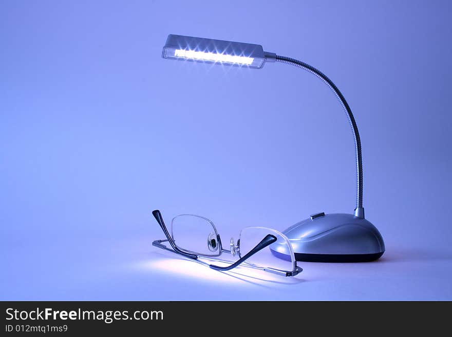 Table lamp and modern spectacles lying on blue background. Table lamp and modern spectacles lying on blue background