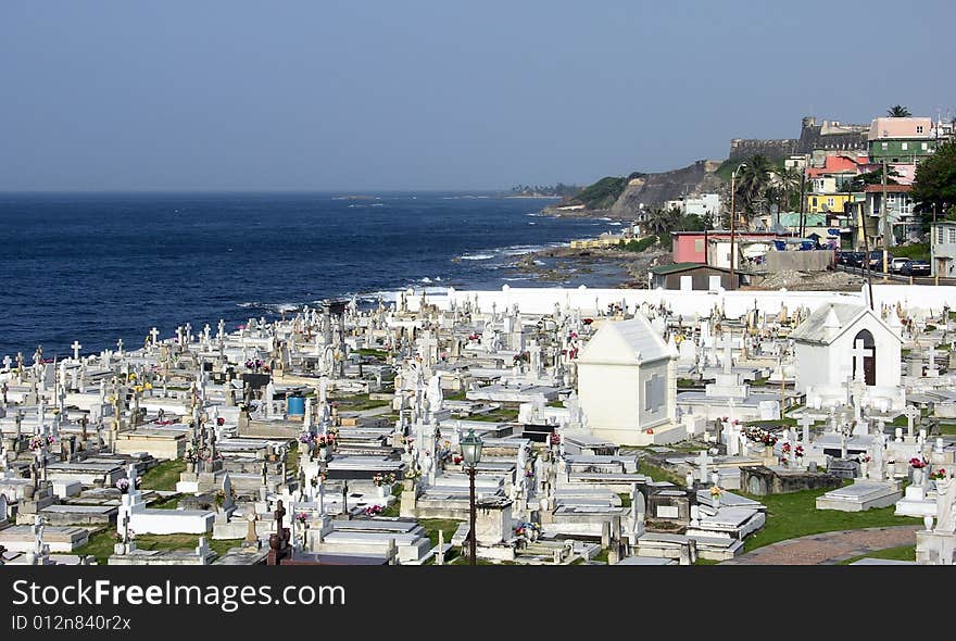 The view of a cemetery by the sea with La Perla district and historic fort in a background in the old city of San Juan, the capital of Puerto Rico. The view of a cemetery by the sea with La Perla district and historic fort in a background in the old city of San Juan, the capital of Puerto Rico.