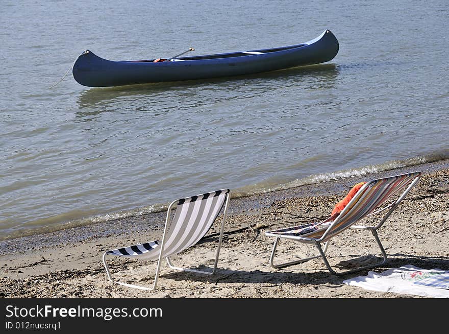 Peaceful deck chairs in bank of a river with a canoe in the background