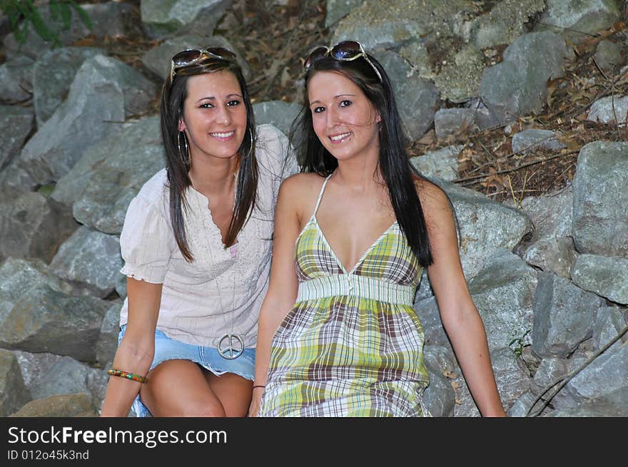 Two young ladies sitting together on the rocks smiling happily. Two young ladies sitting together on the rocks smiling happily.