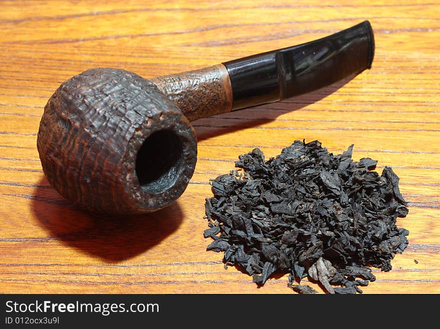 An old tobacco pipe and tobacco on wood background.