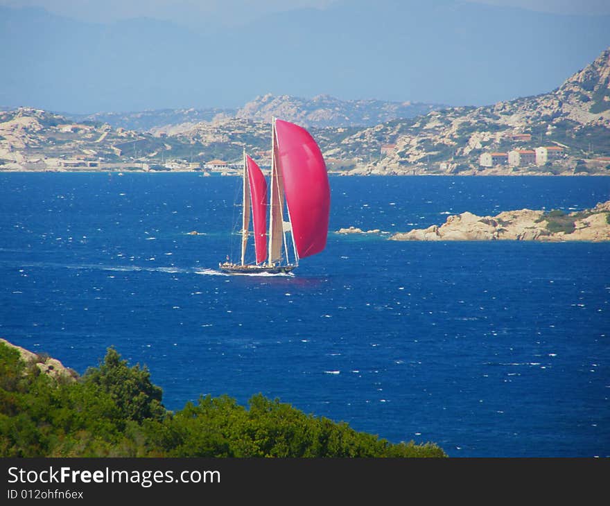 Red sails yacht sailing in the beautiful blue windy sea off the Sardinian coast near Palau, Italy, with wind in its sails