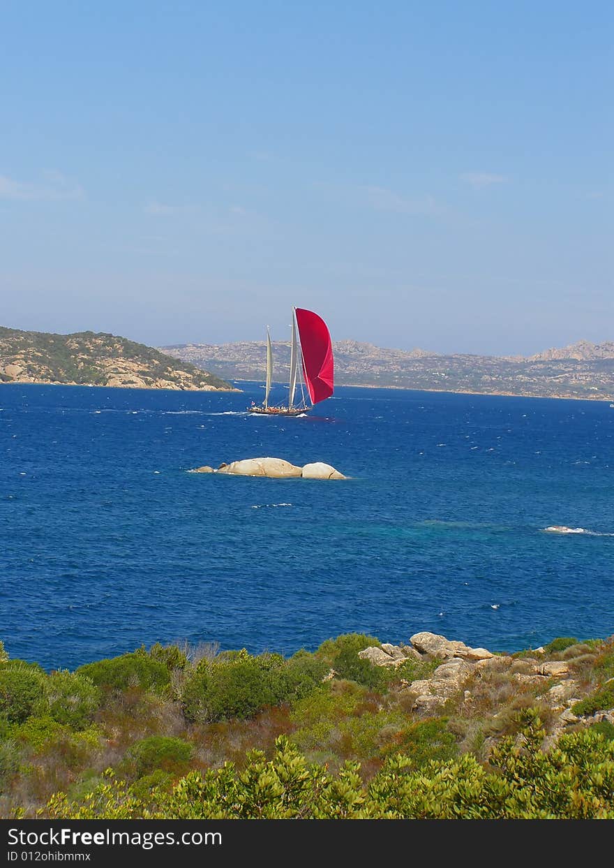 Red sails yacht sailing in the beautiful blue windy sea off the Sardinian coast near Palau, Italy, with wind in its sails