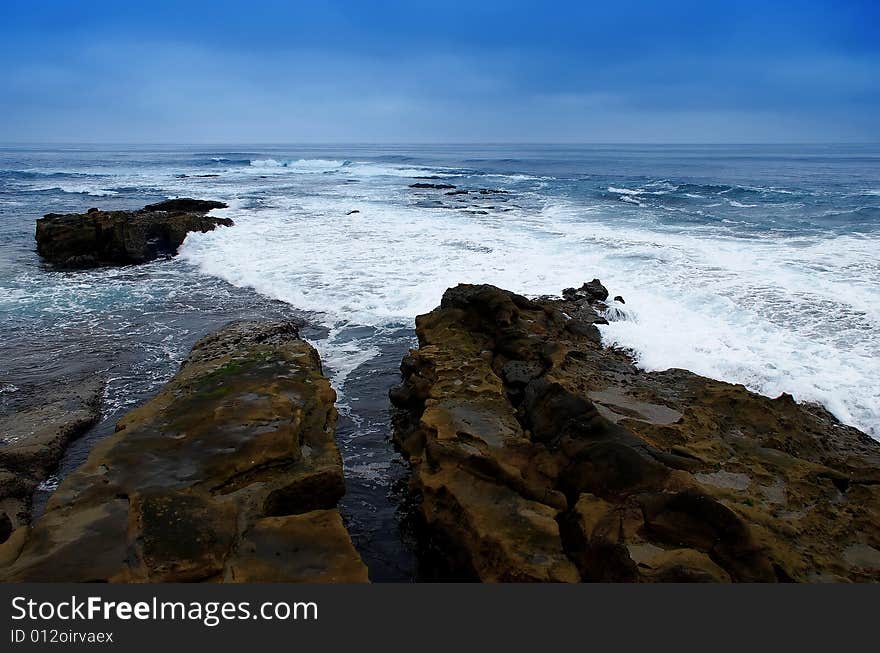 A split rock with waves of white sea foam swirling around them. A split rock with waves of white sea foam swirling around them