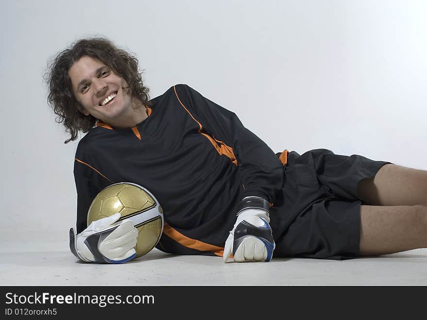 Soccer player lying on his side smiling and holding a soccer ball. Horizontally framed photograph. Soccer player lying on his side smiling and holding a soccer ball. Horizontally framed photograph