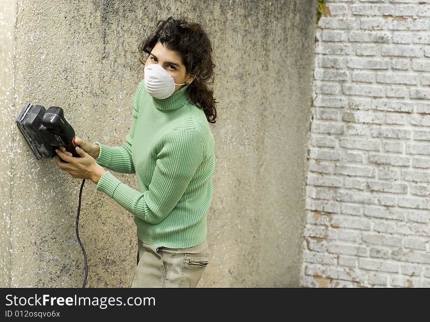 Woman wearing a mask using an electric sander. Horizontally framed photo. Woman wearing a mask using an electric sander. Horizontally framed photo.