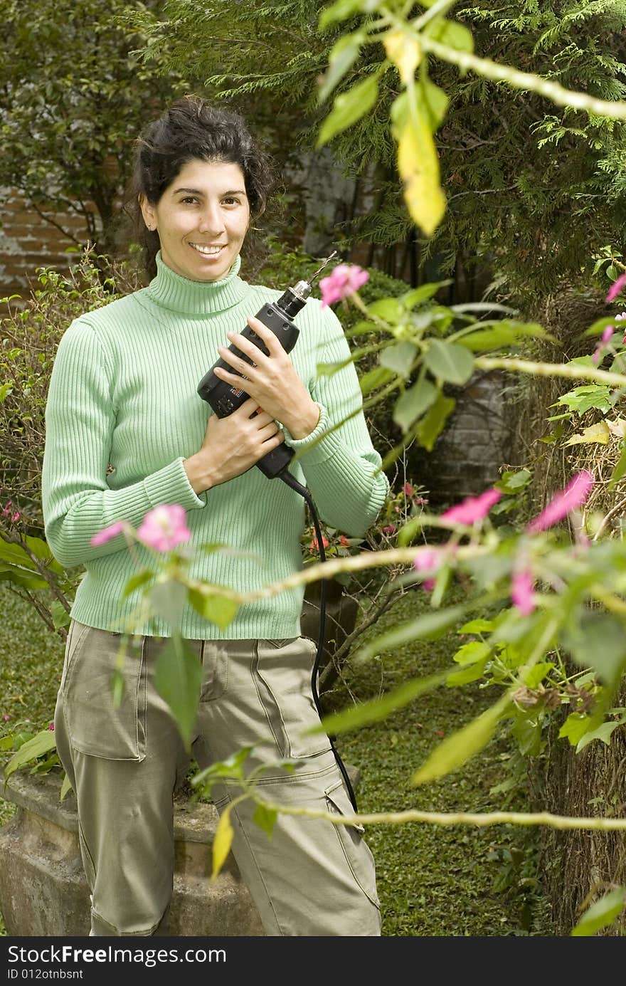 Smiling woman holding a drill by some flowers. Vertically framed photo. Smiling woman holding a drill by some flowers. Vertically framed photo.