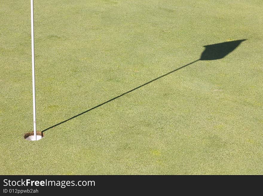 Hole and shadow of a golf green flag on the green