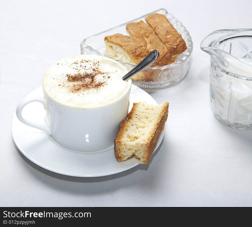 Coffee in white cup with spoon and caramal rusk, more rusks and milk in background. Coffee in white cup with spoon and caramal rusk, more rusks and milk in background