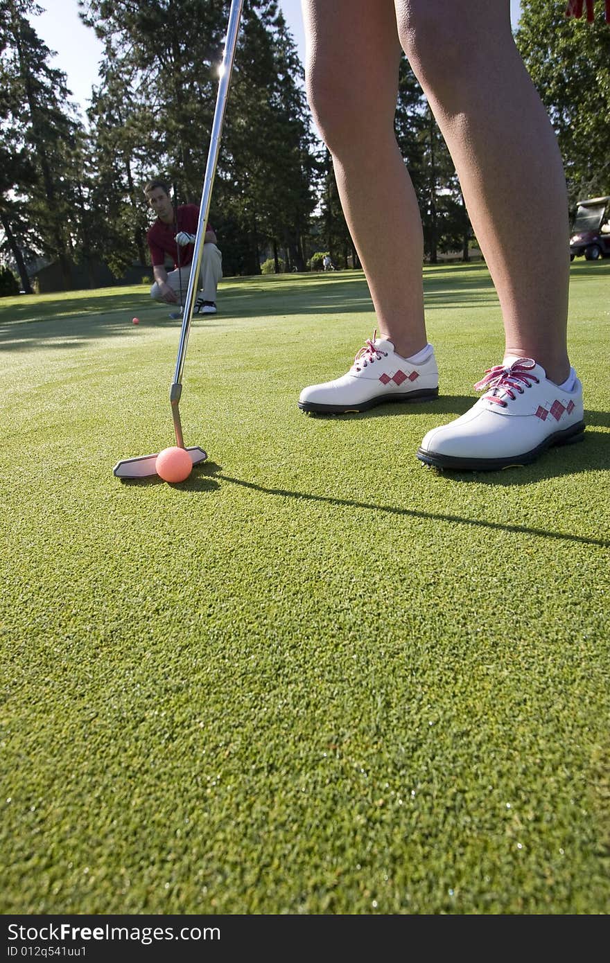 A woman is standing on the green of a golf course.  She is about to putt the ball into the hole.  Vertically framed shot. A woman is standing on the green of a golf course.  She is about to putt the ball into the hole.  Vertically framed shot.