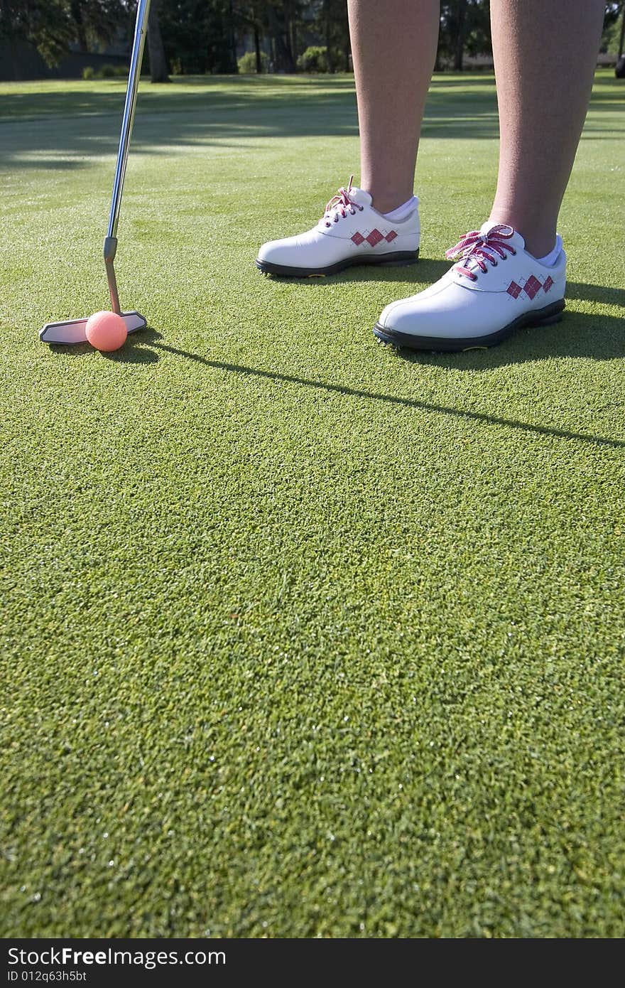 A woman is standing on the green of a golf course.  She is about to putt the ball into the hole.  Vertically framed shot. A woman is standing on the green of a golf course.  She is about to putt the ball into the hole.  Vertically framed shot.