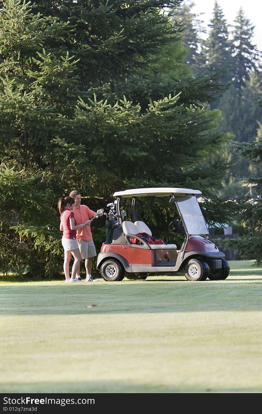 A happy couple standing near their golf cart inspect their golf clubs. Vertically framed photo. A happy couple standing near their golf cart inspect their golf clubs. Vertically framed photo