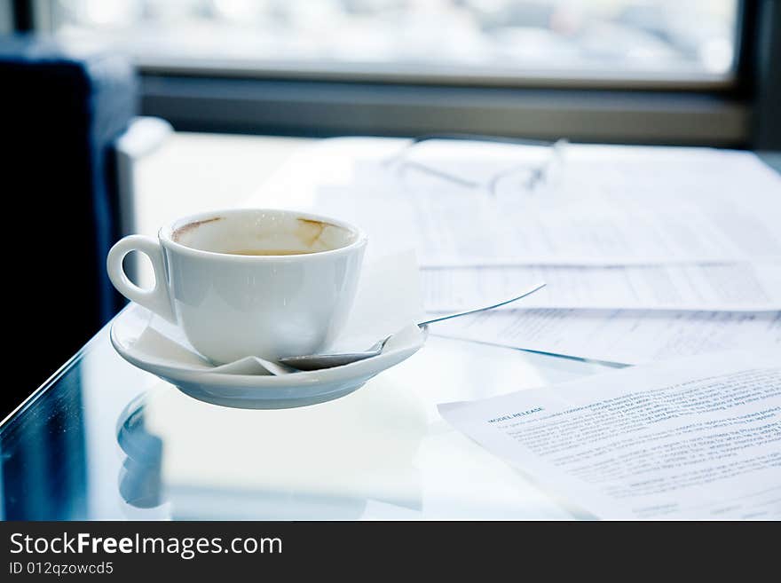 A cup of coffee, eyeglasses and papers lying on the table. A cup of coffee, eyeglasses and papers lying on the table