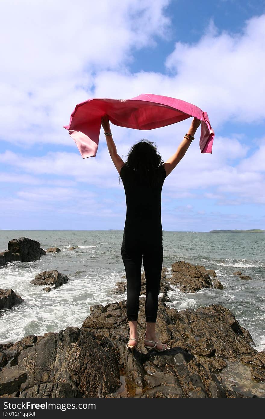 Woman with high heels on the rocks at the waters edge happily waving a silk scarf in the air. Woman with high heels on the rocks at the waters edge happily waving a silk scarf in the air