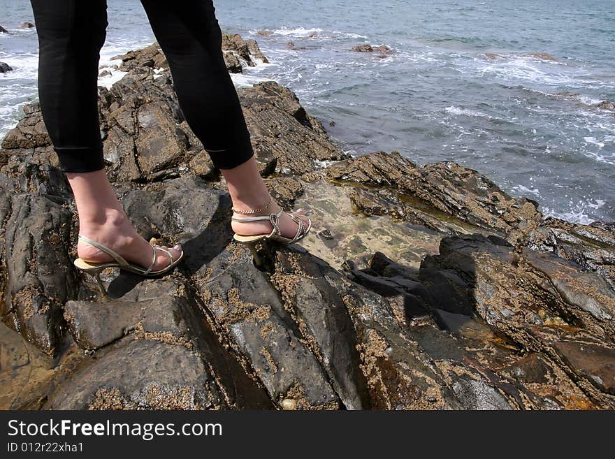 Woman with high heels on the rocks at the waters edge