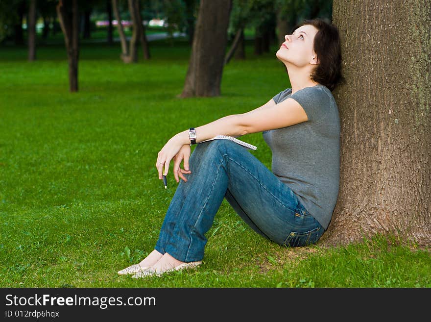 Girl sits under a tree with a thoughtful kind