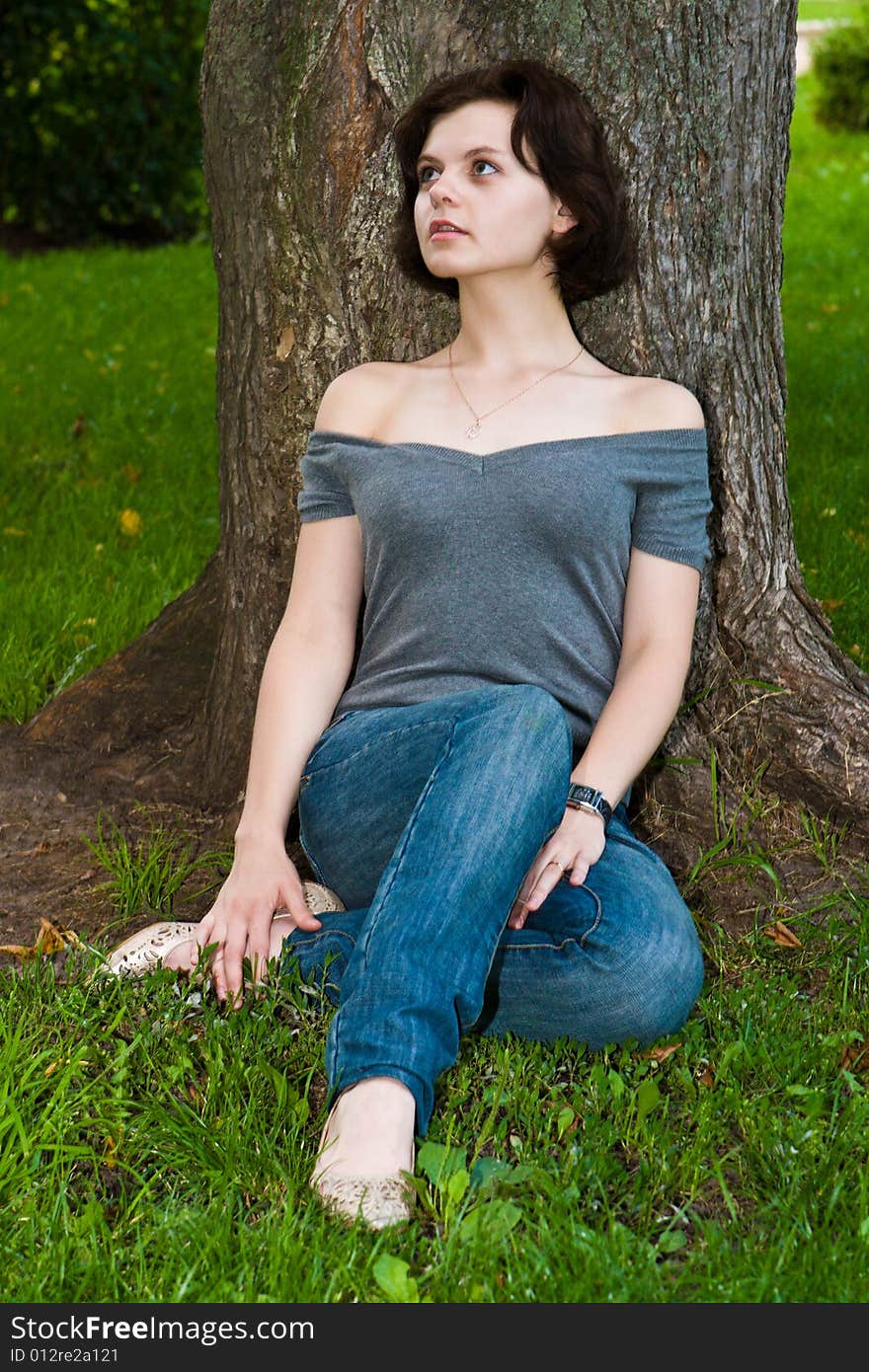 Beautiful girl has a rest sitting on a grass under a tree. Beautiful girl has a rest sitting on a grass under a tree