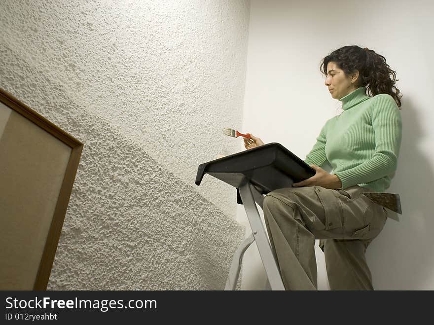 Woman paints a wall while standing on a ladder - Horizontally framed photo. Woman paints a wall while standing on a ladder - Horizontally framed photo