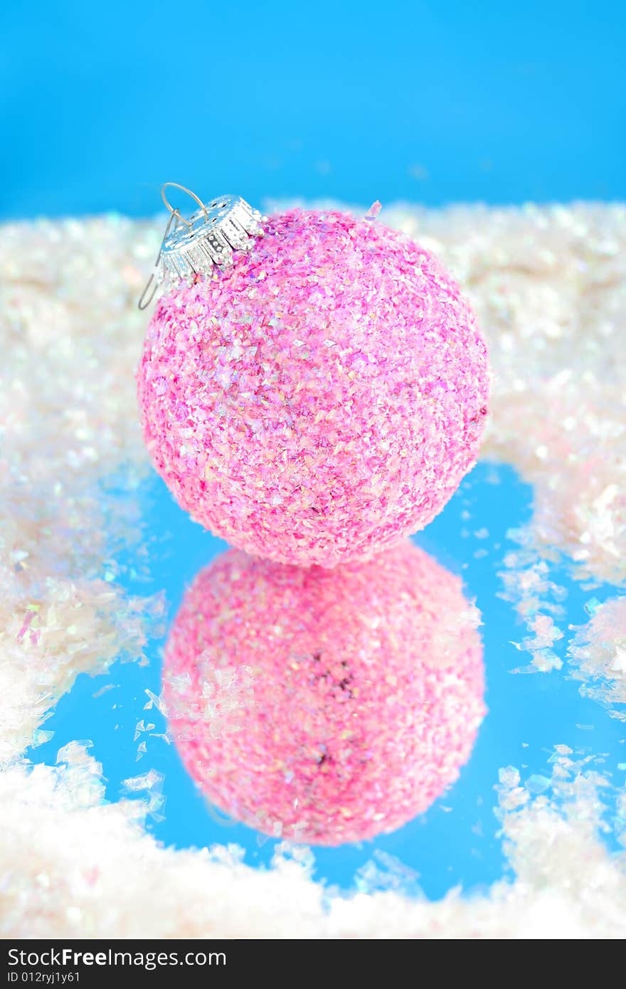 Pink sparkly christmas ball with reflection on blue surrounded by fake snow. Pink sparkly christmas ball with reflection on blue surrounded by fake snow