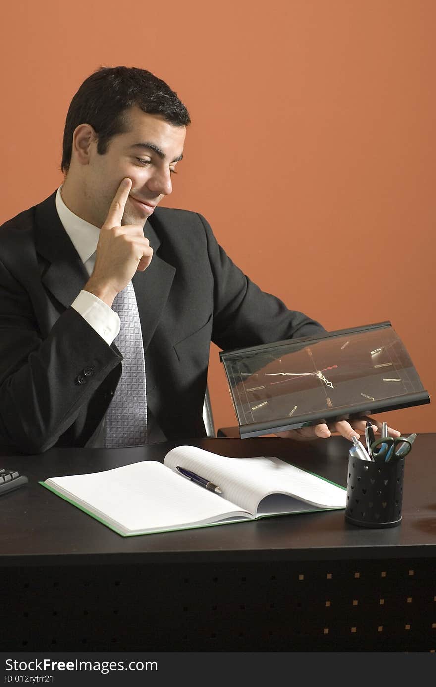 Business man smiles as he sits at his desk looking at his clock. Vertically framed photo. Business man smiles as he sits at his desk looking at his clock. Vertically framed photo.