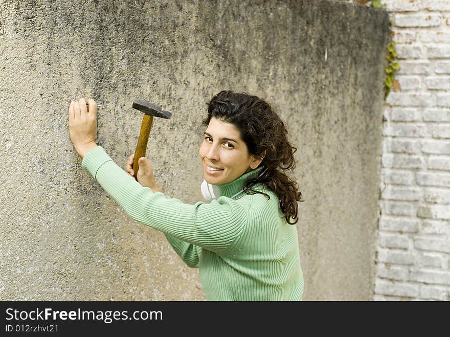 Woman smiling as she hammers a nail into a wall. Horizontally framed photo. Woman smiling as she hammers a nail into a wall. Horizontally framed photo.