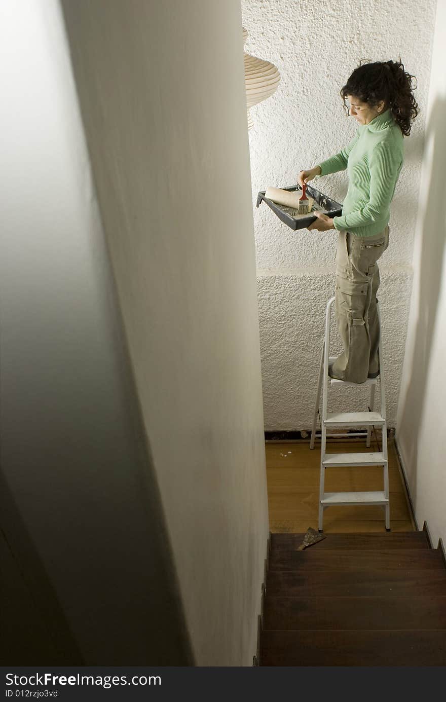 Woman standing on a ladder holding a paint roller and tray. Vertically framed photo. Woman standing on a ladder holding a paint roller and tray. Vertically framed photo.