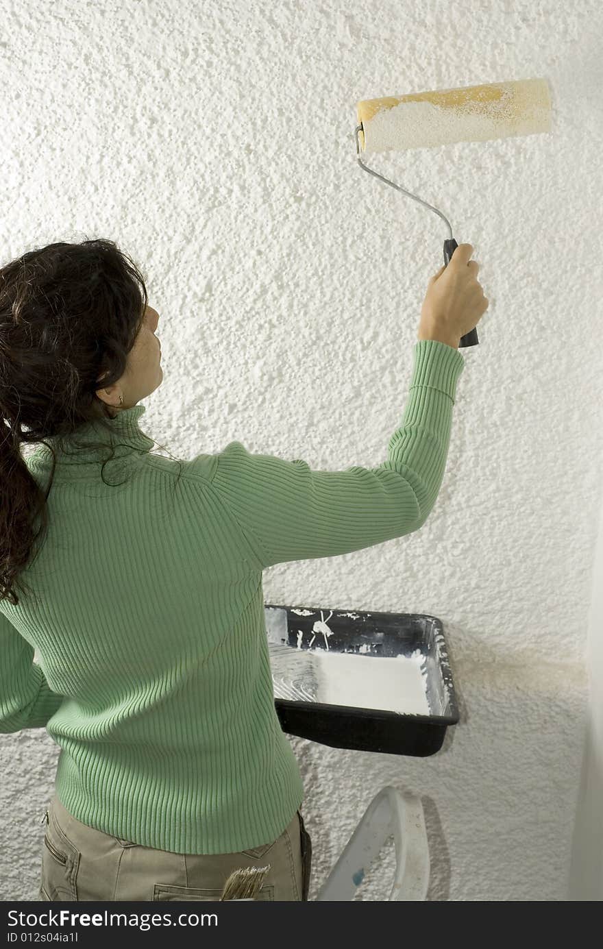 Woman uses a paint roller to paint a wall. Vertically framed photo. Woman uses a paint roller to paint a wall. Vertically framed photo.