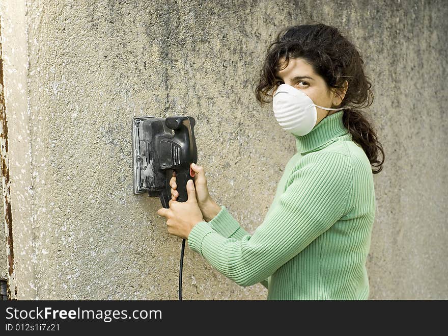 Woman wearing a mask using an electric sander. Horizontally framed photo. Woman wearing a mask using an electric sander. Horizontally framed photo.