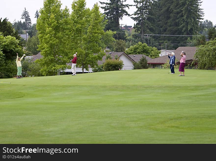 Group of four women celebrating with their arms up while playing golf. Horizontally framed photo. Group of four women celebrating with their arms up while playing golf. Horizontally framed photo.