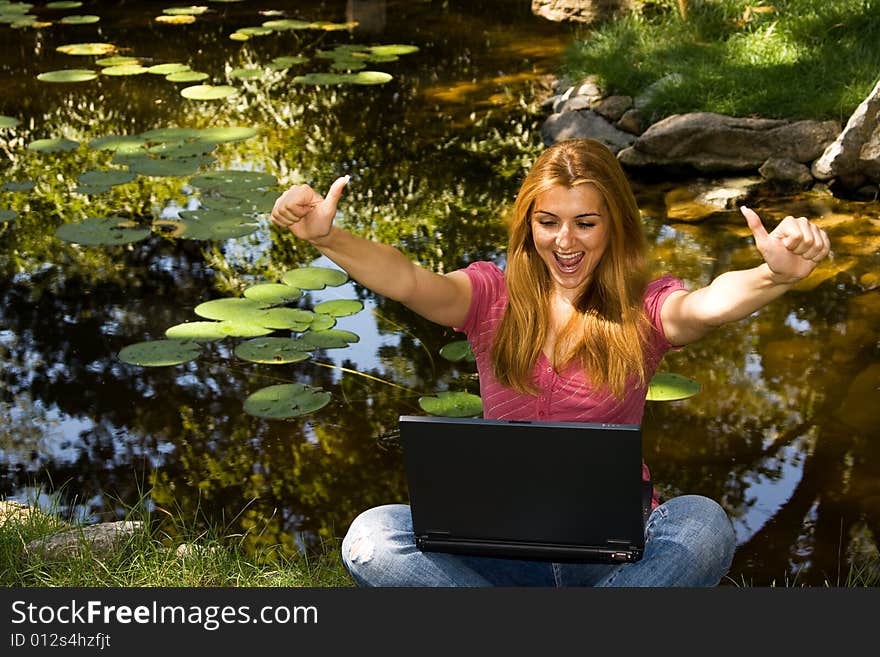 Happy beautiful student using laptop near water in park.