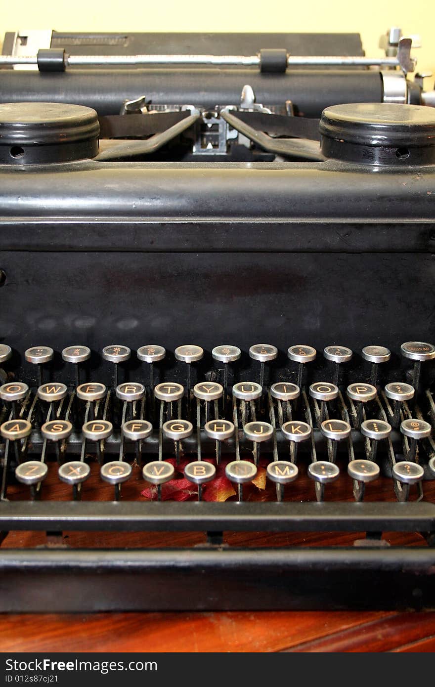 An antique typewriter sits on a wooden table against a yellow wall.