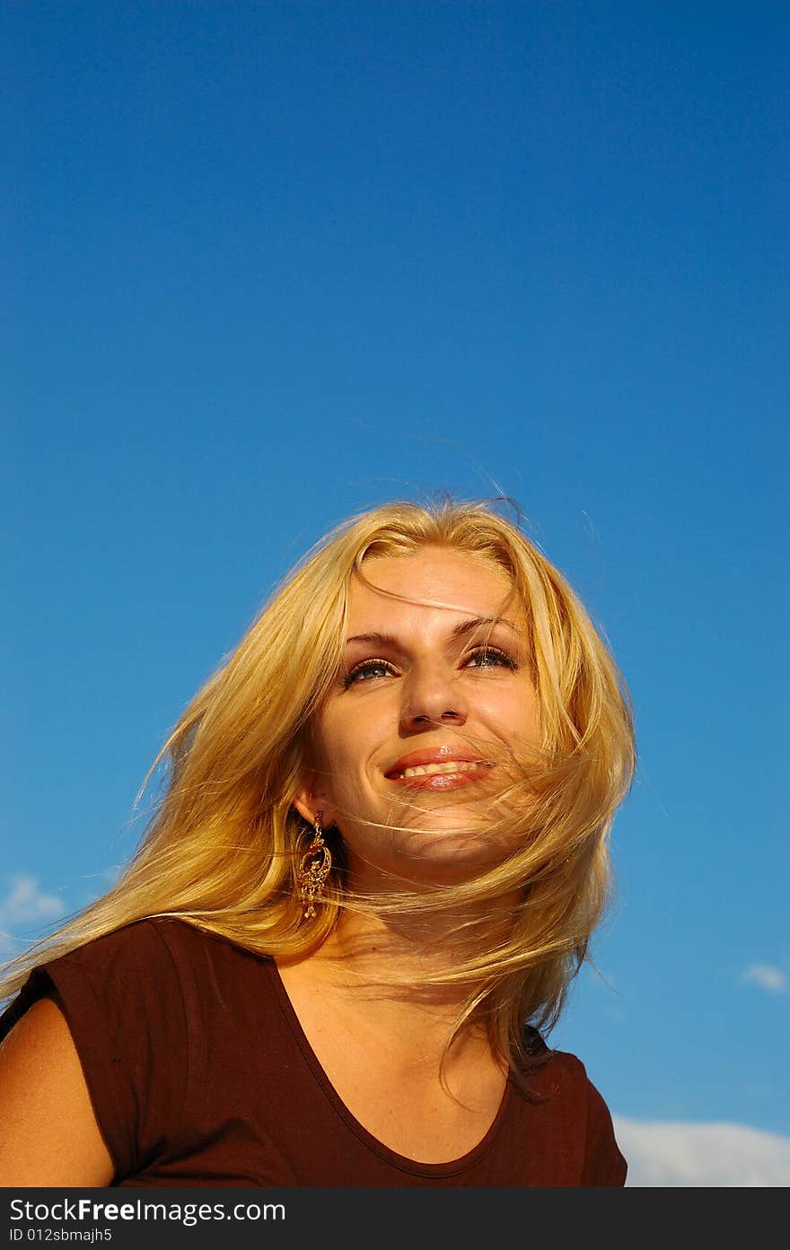 Smiling blond woman with fly-away hair against blue sky. Smiling blond woman with fly-away hair against blue sky