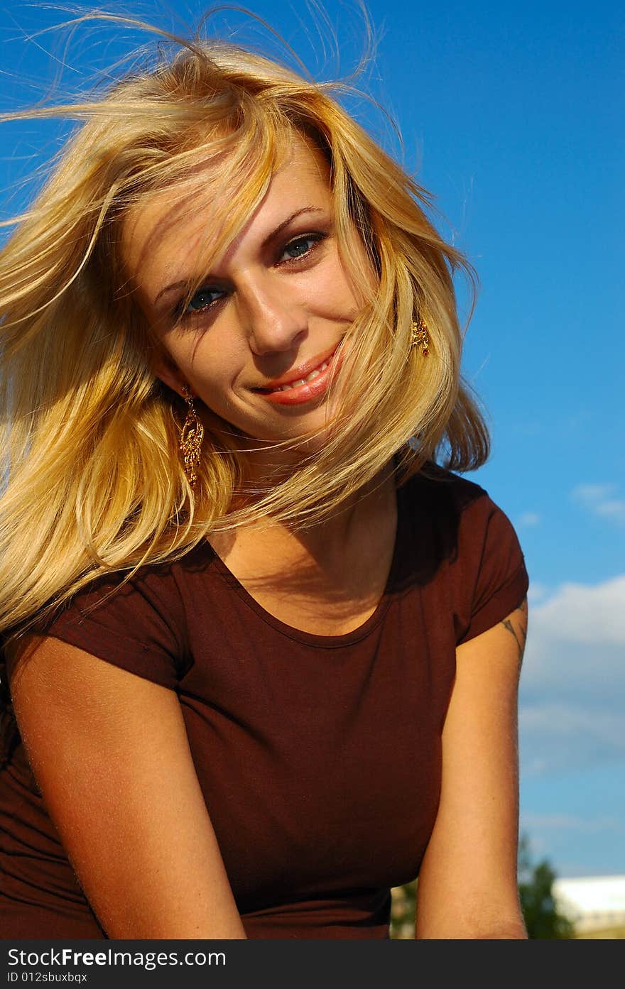 Smiling blond woman with fly-away hair against blue sky. Smiling blond woman with fly-away hair against blue sky